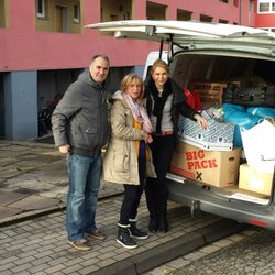 Drei Personen vor der aufgeklappten Heckklappe eines Lieferwagens, gefüllt mit Spendenartikeln