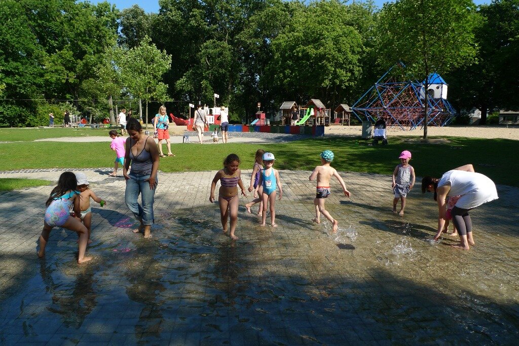 Kinder und ihre Erzieherinnen planschen im Wasserbecken auf dem Spielplatz