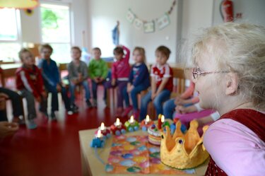 Kindergruppe feiert Geburtstag - Stuhlkreis im Hintergrund, vorne ein Mädchen am Geburtstagstisch