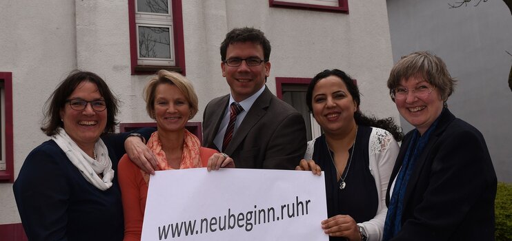 Eine Gruppe von Frauen und Männern hält ein Plakat mit der Aufschrift www.neubginn.ruhr in die Kamera