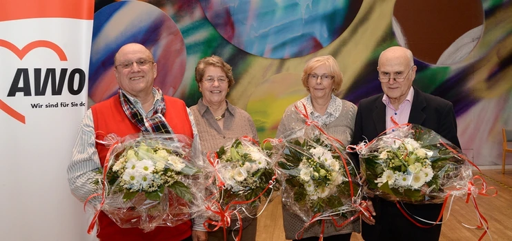 Gruppenbild der neuen und ausscheidenden Vorsitzenden vor einer bunten Wand. Links ein AWO-Banner. Alle Personen halten Blumensträuße in der Hand.