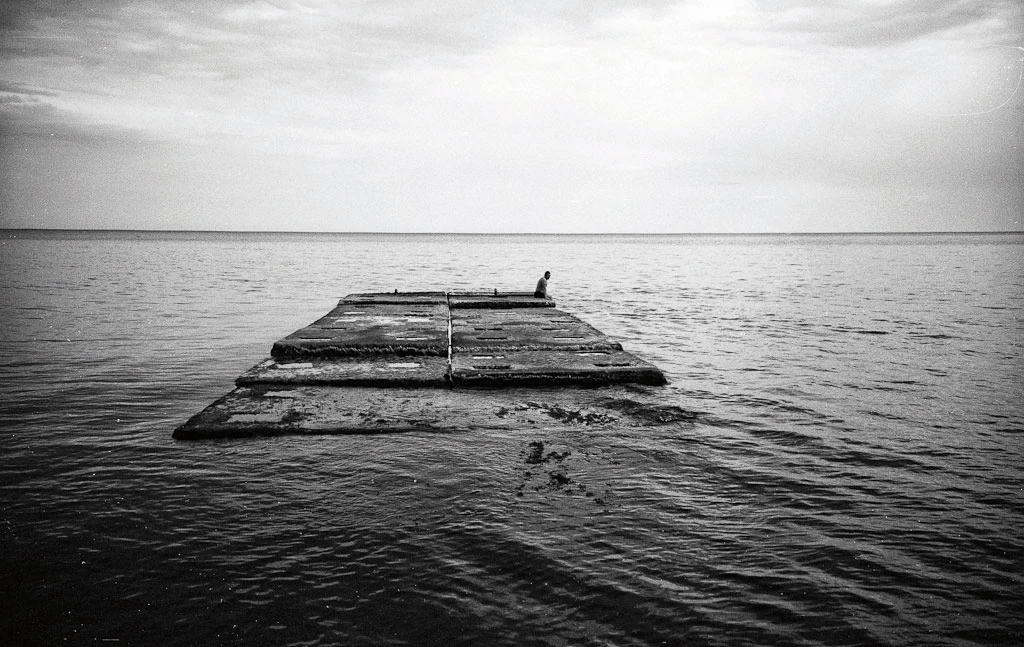 Ein Mann sitzt, mit den Beinen im Wasser, auf einem Plateau im Meer.