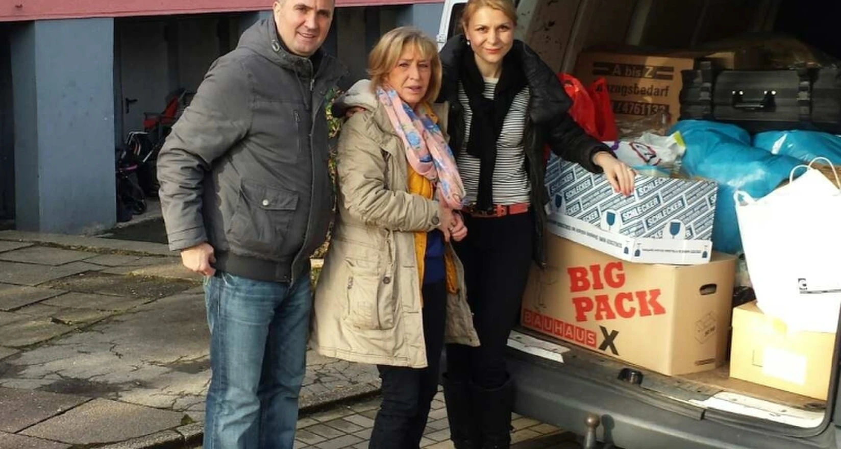 Drei Personen vor der aufgeklappten Heckklappe eines Lieferwagens, gefüllt mit Spendenartikeln