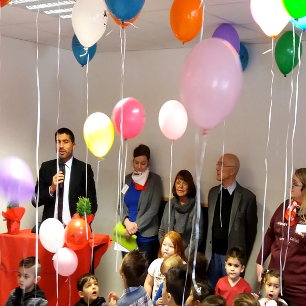 Grußworte des Vorsitzenden an die Gäste der Kita-Eröffnungsfeier. Im Vordergrund Kinder, dahinter erwachsene Gäste. Luftballons schweben unter der Decke.