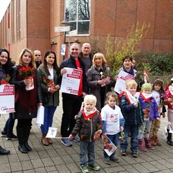 Menschengruppe (Mann, Frauen und Kinder) mit Plakaten "Gegen rassismus" und Rosen in der Hand vor einem Gebäude.