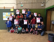 Eine Menschengruppe vor einer Hallenwand mit Plakaten "AWO gegen Rassismus"