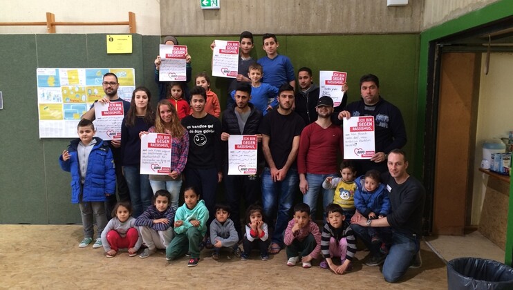 Eine Menschengruppe vor einer Hallenwand mit Plakaten "AWO gegen Rassismus"