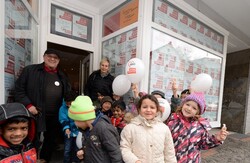 Zwei Erwachsene und eine Kindergruppe im Eingang des AWO Stadtbüros. Im Hintergrund die Fensterfronten mit Plakaten gegen Rassismus.