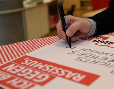 Eine Hand mit Stift schreibt einen Text auf ein Plakat mit dem Aufdruck AWO gegen Rassismus