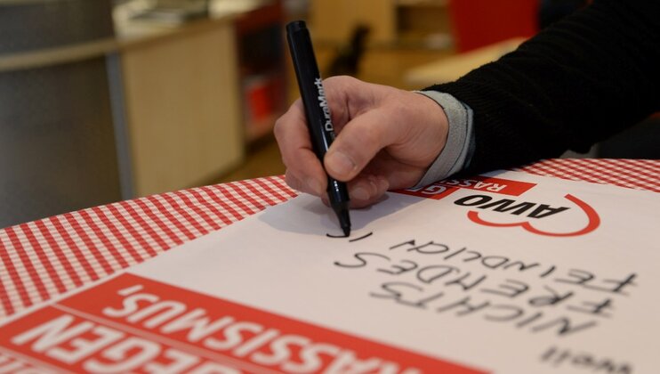Eine Hand mit Stift schreibt einen Text auf ein Plakat mit dem Aufdruck AWO gegen Rassismus