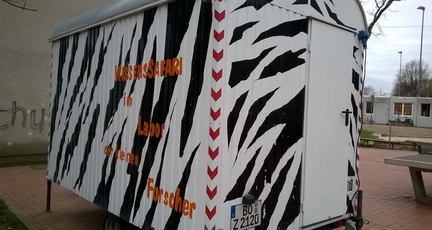 Ein schwarz-weiß angestrichener Bauwagen mit der Aufschrift Wissenssafari im Labor der kleinen Forscher