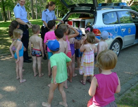 Kindergruppe schaut in den Kofferraum eines Polizeiautos, zwei Polizistinnen stehen dabei