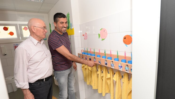 Zwei Männer begstaunen die Kinderbilder an den Wanfhaken im Waschraum - Vorsitzender Heinz Drenseck und Landtagsabgeordneter Serdar Yüksel