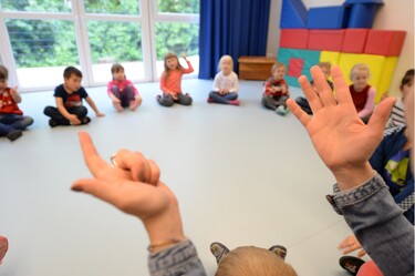 Kinder beim Kreisspiel, im Vordergrund die Hände der Erzieherin