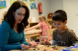 Leiterin Anke Heesen spielt mit einem Kitakind ein Brettspiel