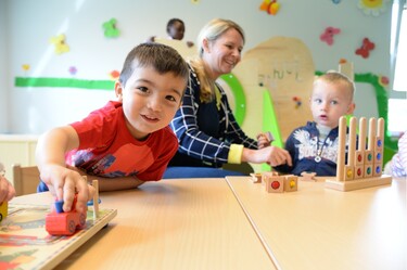 Zwei Jungen und eine Erzieherin spielen am Tisch