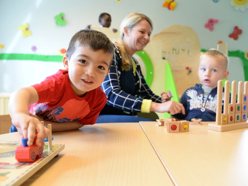 Zwei Jungen und eine Erzieherin spielen am Tisch