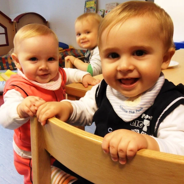 Drei kleine unter dreijährige Kinder im Gruppenraum, alle lachen dem Fotografen zu