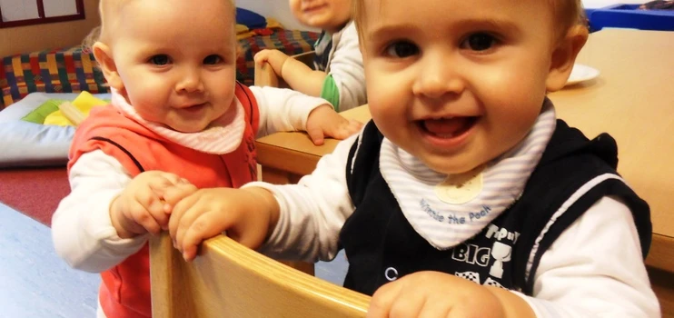 Drei kleine unter dreijährige Kinder im Gruppenraum, alle lachen dem Fotografen zu