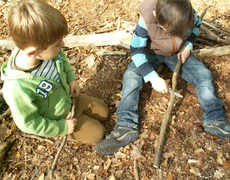 Zwei Jungen sitzen auf dem Waldboden, einer schnitzt an einem Ast