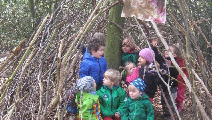 Kinder im wald unter aufgeschichteten Ästen mit einer selbst bemalten Fahne