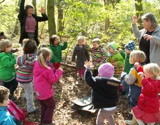 Eine Kindergruppe und zwei Frauen tanzen im Wald den Indianertanz