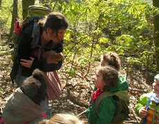 Eine Frau und Kinder im Wald - die Frau macht ewas vor und die Kinder hören lachend zu