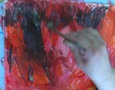 Eine Hand in Bewegung pinselt an einem Bild mit roten und schwarzen Farben