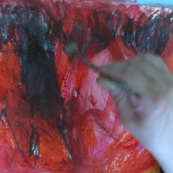 Eine Hand in Bewegung pinselt an einem Bild mit roten und schwarzen Farben