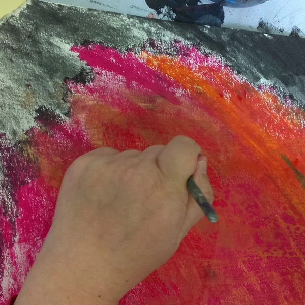 Eine Hand mit einem Farbstift malt an einem Bild mit kräftigen Farben in rot, orange und schwarz