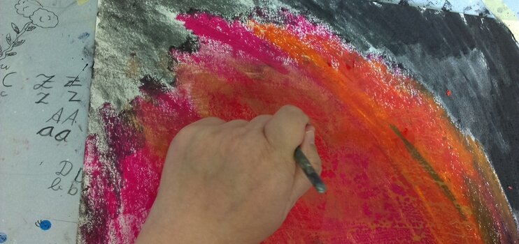Eine Hand mit einem Farbstift malt an einem Bild mit kräftigen Farben in rot, orange und schwarz