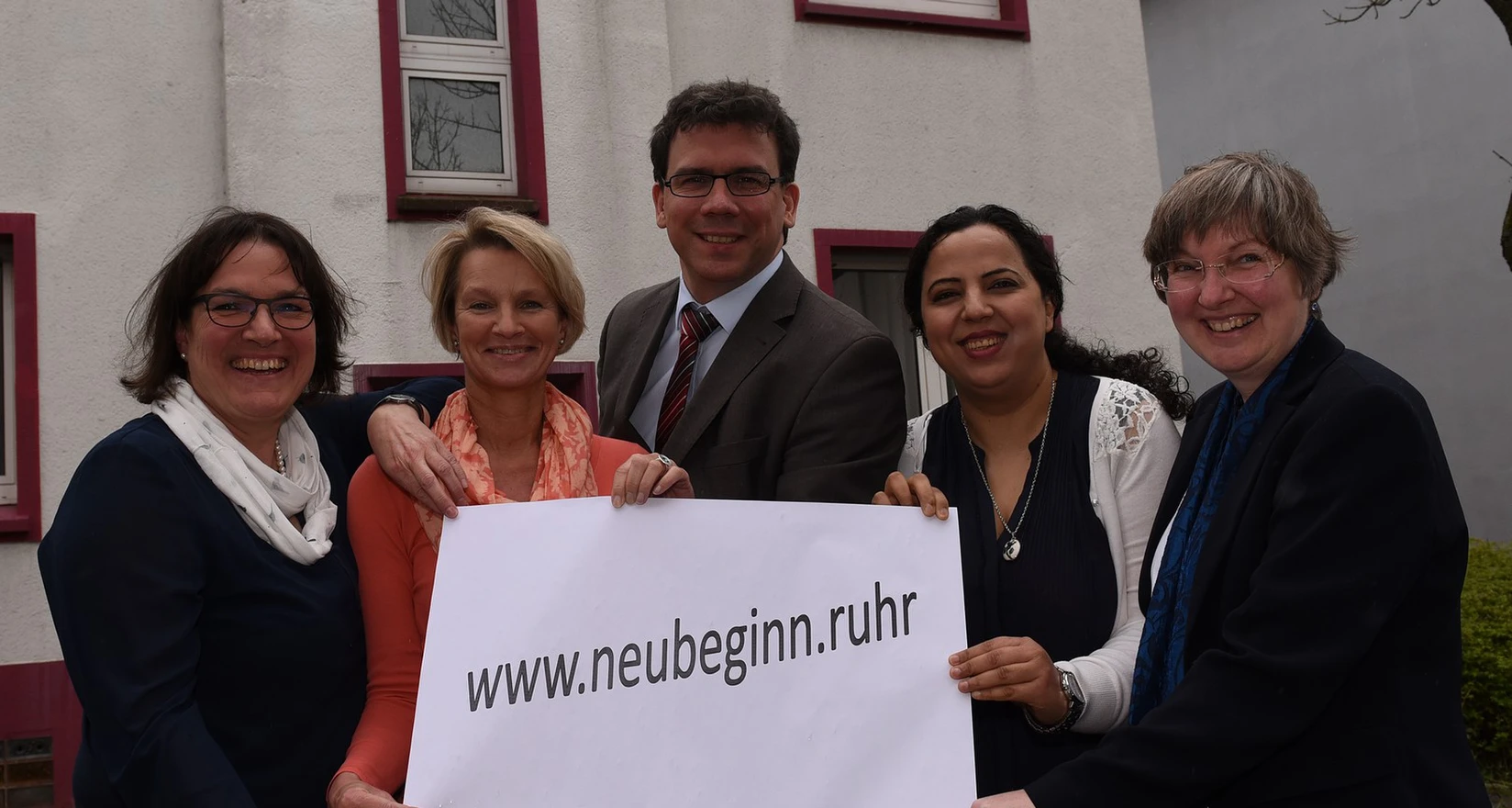 Eine Gruppe von Frauen und Männern hält ein Plakat mit der Aufschrift www.neubginn.ruhr in die Kamera
