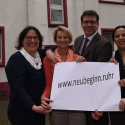 Eine Gruppe von Frauen und Männern hält ein Plakat mit der Aufschrift www.neubginn.ruhr in die Kamera