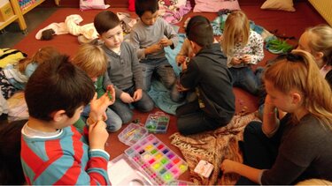 Eine Gruppe von Mädchen und Jungen knien auf dem Teppich und spielen mit Perlen