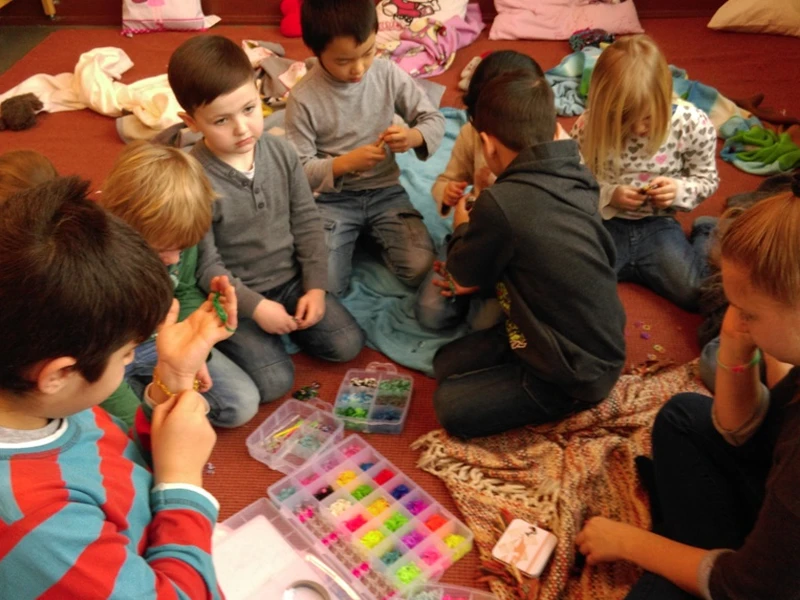 Eine Gruppe von Mädchen und Jungen knien auf dem Teppich und spielen mit Perlen