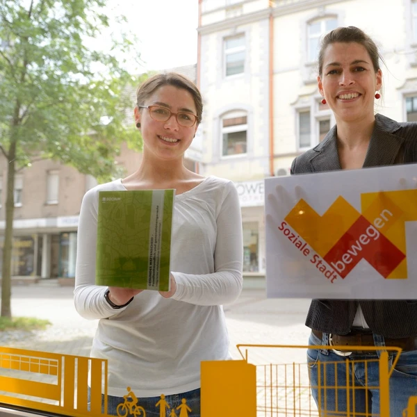 Zwei Frauen vor der Schaufensterscheibe zeigen die Signets des Projektes Stadtteilerneuerung