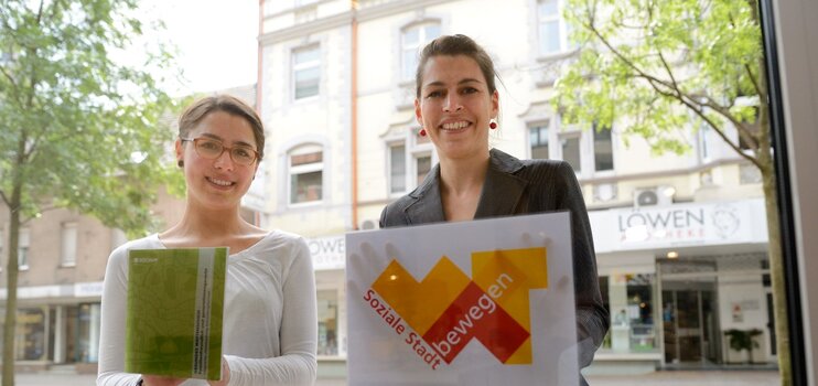Zwei Frauen vor der Schaufensterscheibe zeigen die Signets des Projektes Stadtteilerneuerung