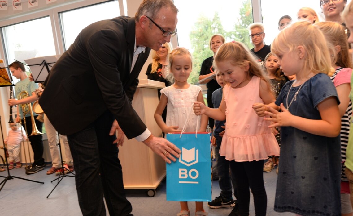 Ein Vertreter der Stadt Bochum überreicht drei kleinen Mädchen eine Tüte mit dem Logo der Stadt