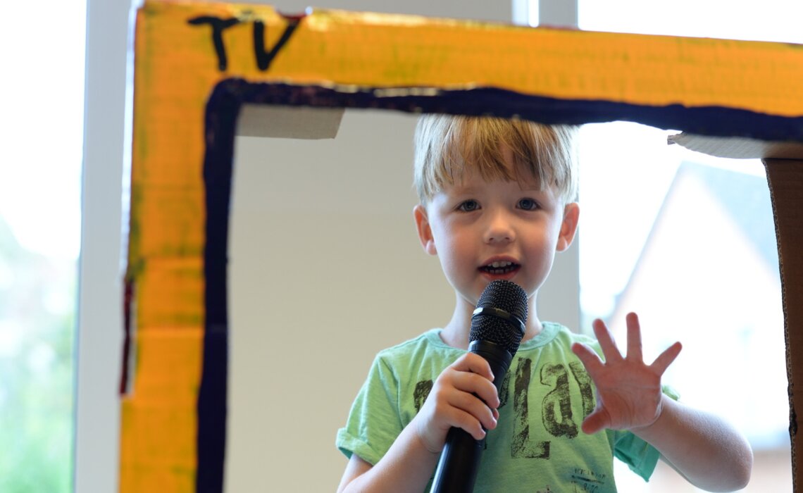 Junge mit Mikrofon im Papp-Fernseher