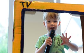 Junge mit Mikrofon im Papp-Fernseher