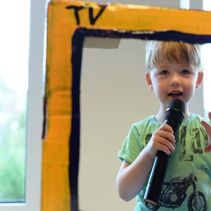 Junge mit Mikrofon im Papp-Fernseher