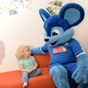 Eine Riesenmaus mit blauem Fell neben einem kleinen Mädchen auf dem sofa
