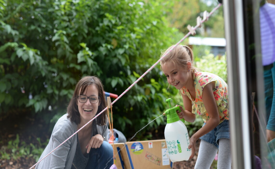 Lachende Frau und Mädchen mit Wasserspritzflasche