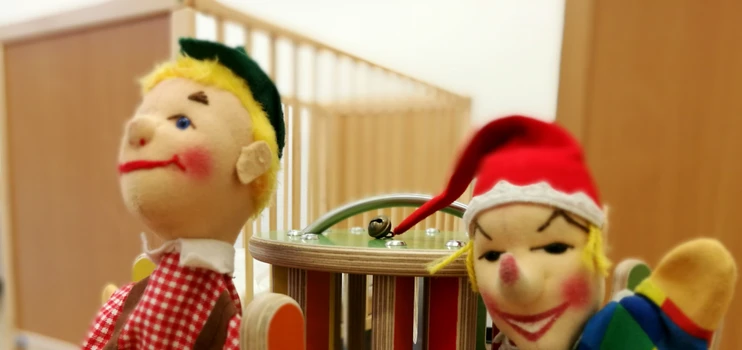 Bunte Kasperfiguren vor Gitterkinderbettchen