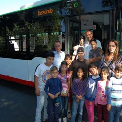 Menschengruppe (Erwachsenen und Kinder) vor einem Bus mit der Aufschrift Busschule