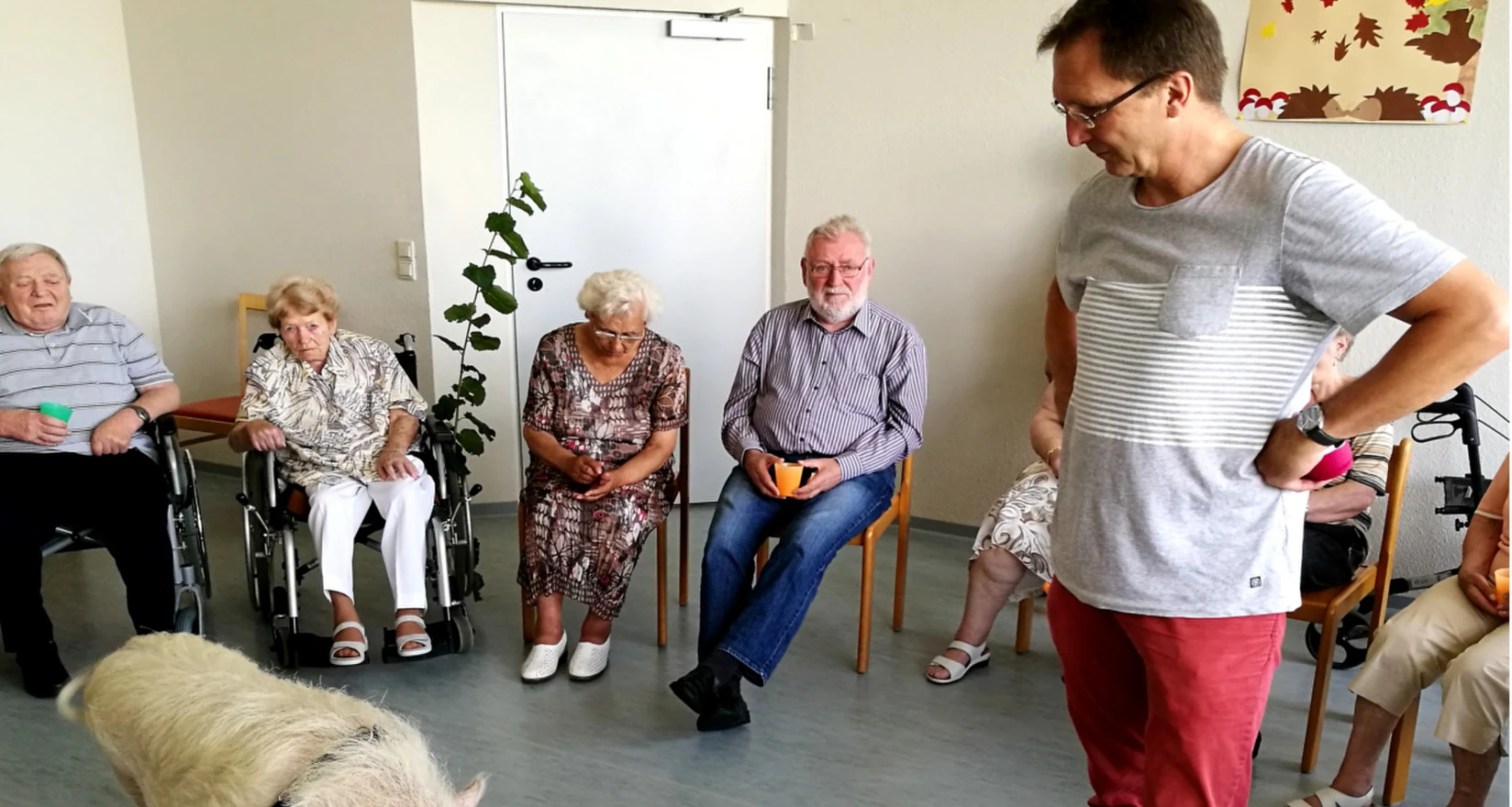 Ein Minischwein mit seinem Betreuer zwischen erstaunten SeniorInnen