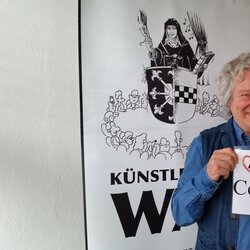 Karikaturist Waldemar Mandzel und Gabriela Osterkamp vor einem Banner des Künstlertreff WAT. Sie halten ein Bild mit der Aufschrift CentrumCultur in die Kamera.