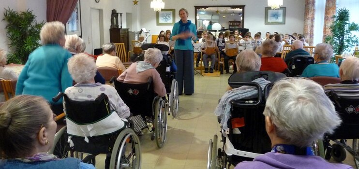 Schulkinder mit ihren Musikinstrumenten spielen für die Senioren im Rollstuhl