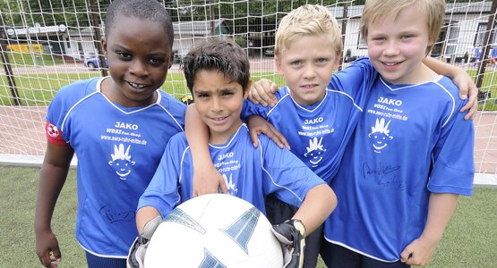 Vier Kinder in Fußballtrikots und mit Ball vor einem Fußballtor
