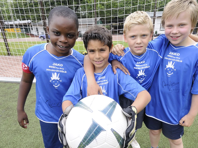 Vier Kinder in Fußballtrikots und mit Ball vor einem Fußballtor